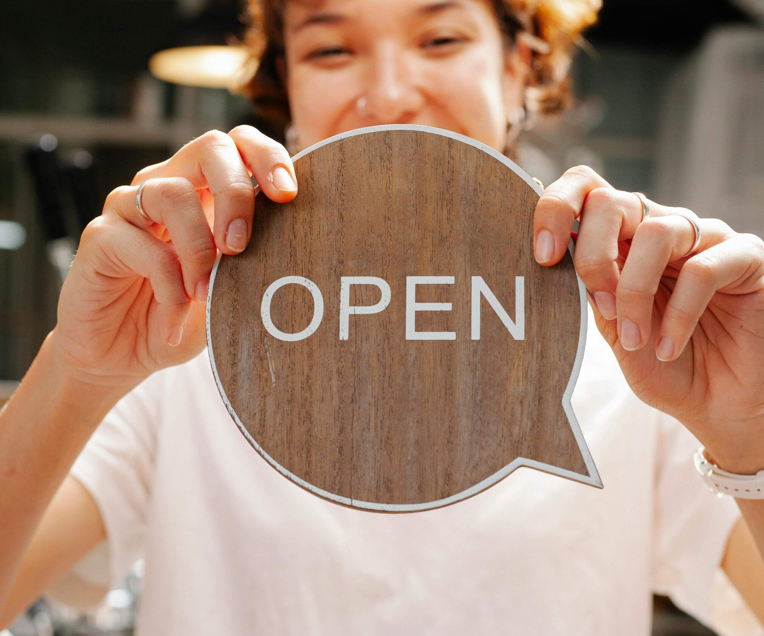 Person holding a wooden sign that says “OPEN,” symbolizing a business opening or welcoming customers