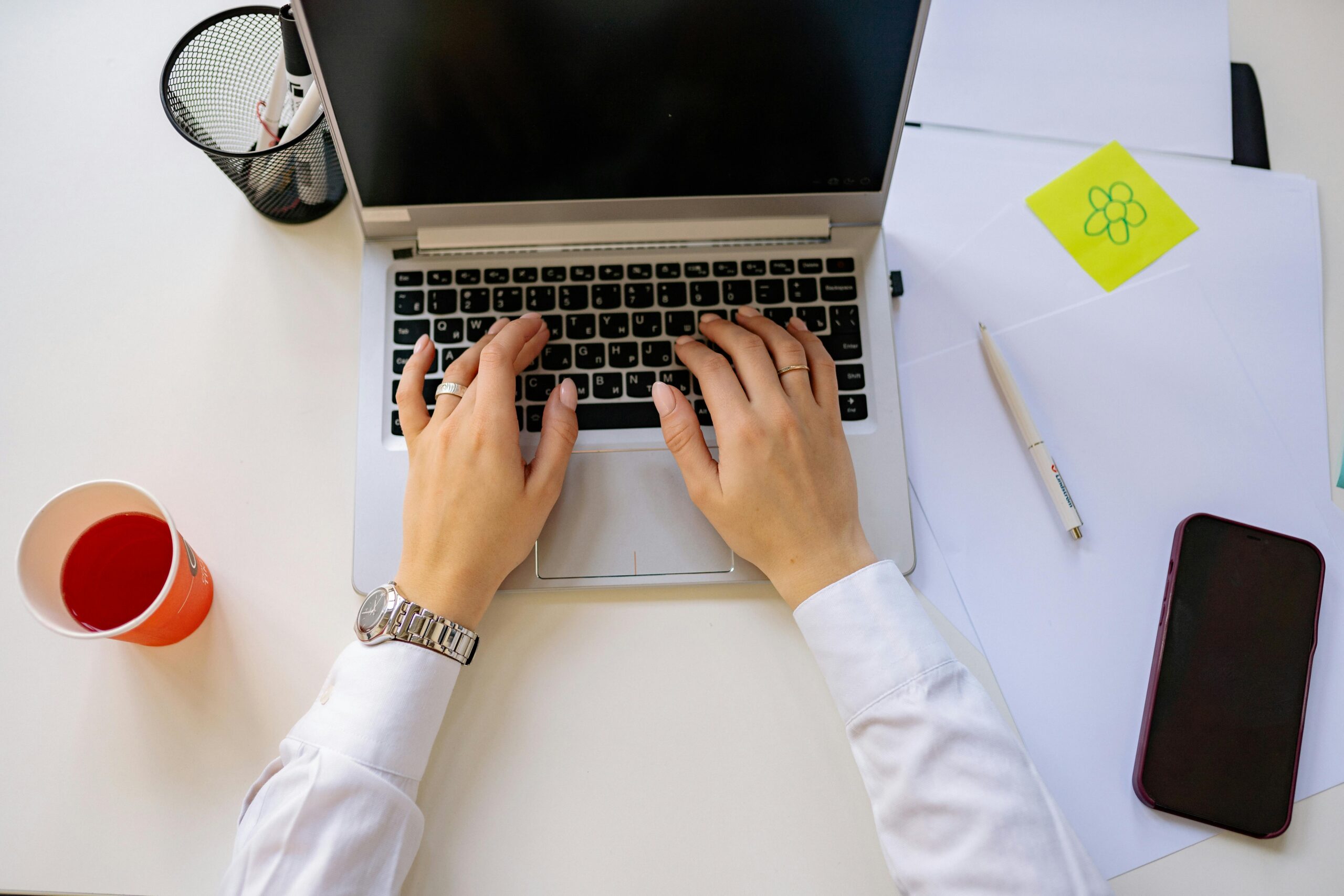 Close-up of a person typing on a laptop at a desk with papers, a pen, smartphone, and a red cup, representing business planning and financial management.