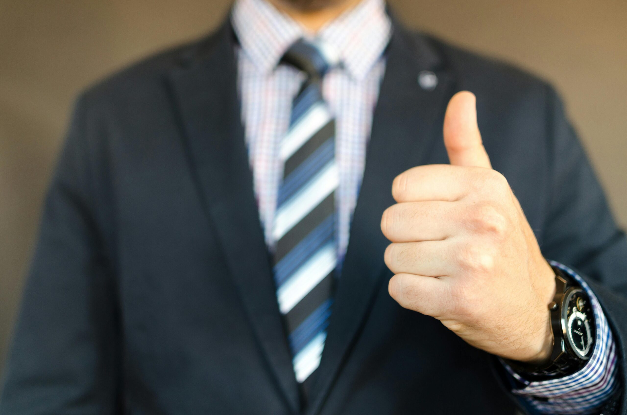 Close-up of a person in a business suit giving a thumbs-up gesture, representing approval, success, or positive business results.