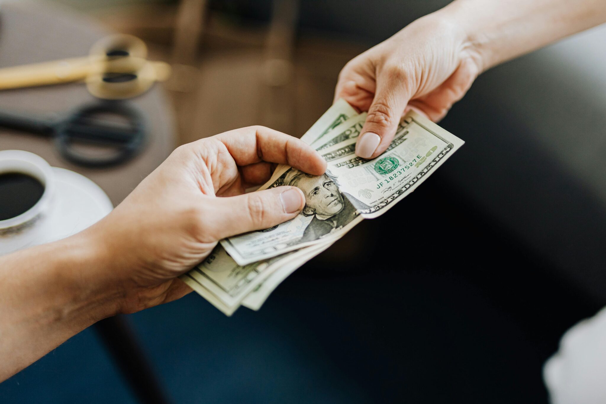 Close-up of one person handing cash in U.S. dollar bills to another person, symbolizing a financial transaction or business funding exchange.
